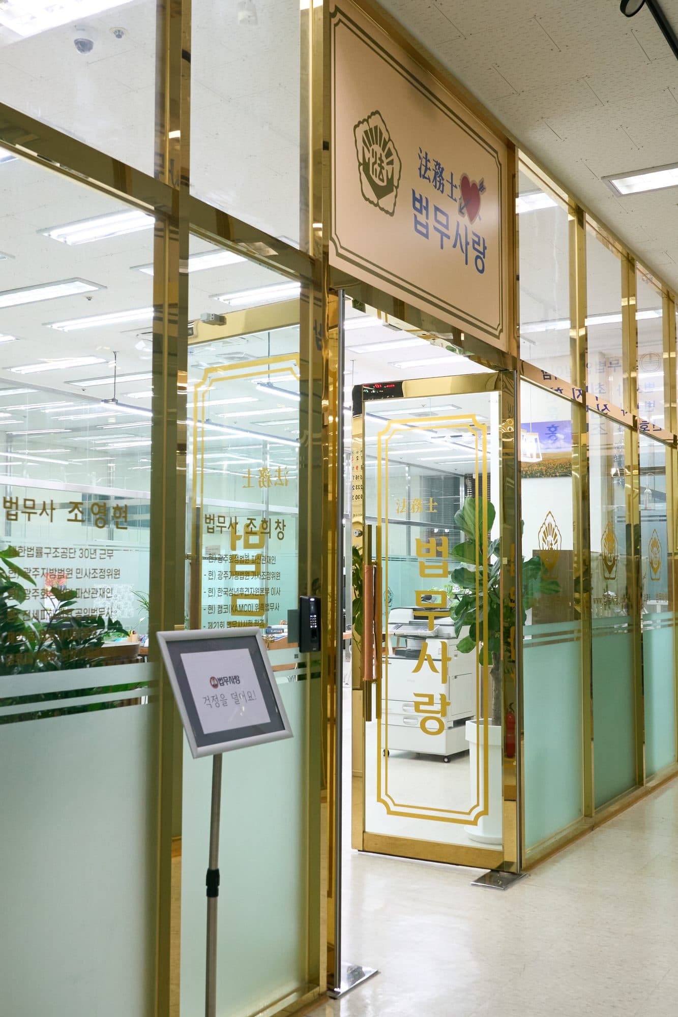 법무사랑 합동사무소 입구. 금색 프레임의 유리문 위에 법무사랑 간판이 걸려 있다.